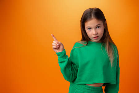 Cute teen girl pointing on copy space behing her back against orange backgroundの写真素材