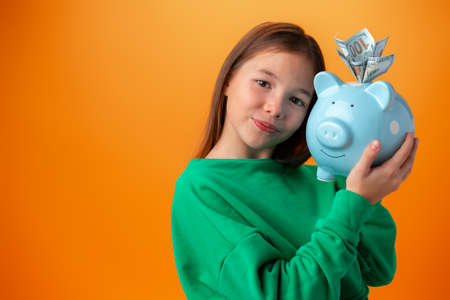 Teen girl with piggy bank on orange color background.の写真素材