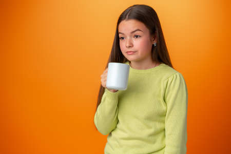 Sleepy teenager girl holding a hot cup of coffee on orange backgroundの写真素材
