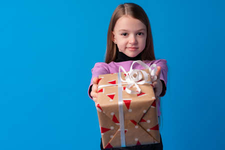 Happy little girl with long hair holding a gift box on a blue backgroundの写真素材