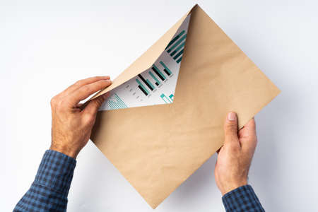 Male hands opening craft paper envelope above white surfaceの写真素材