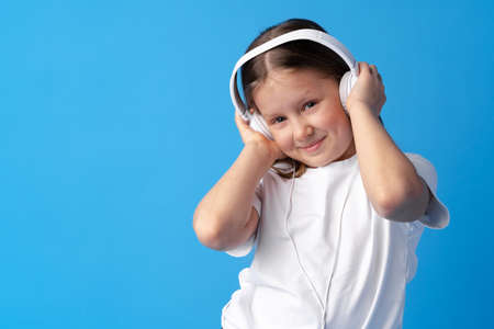 Little girl child wear headphones listen to music over blue backgroundの写真素材