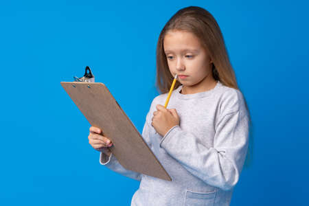 Portrait of little cute girl making notes against blue background