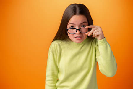 Funny Caucasian teen girl in eyeglasses isolated on orange backgroundの写真素材