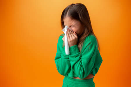 Teen girl blowing her nose against orange backgroundの写真素材