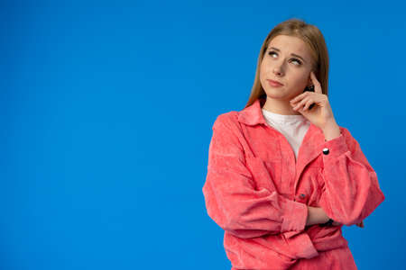 Thoughtful beautiful young woman deep thinking against blue backgroundの写真素材