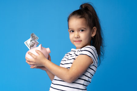 Beautiful little girl with piggy bank on blue backgroundの写真素材