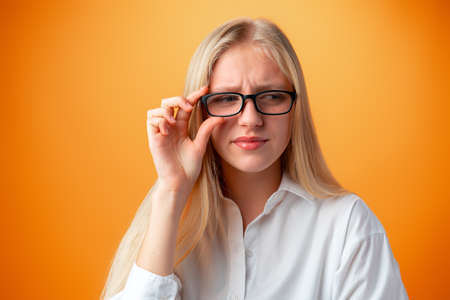 Funny caucasian teen girl in eyeglasses isolated on orange background