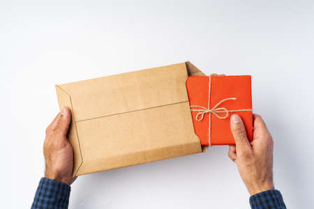 Close up of hands taking gift box out of delivery parcel above white background