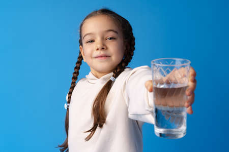 Cute little girl holding glass of water on blue background