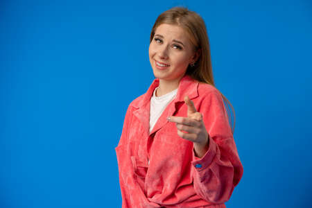 Young woman over blue background points finger at you