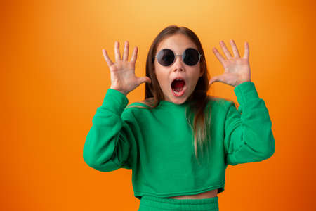 Funny caucasian teen girl in eyeglasses isolated on orange background