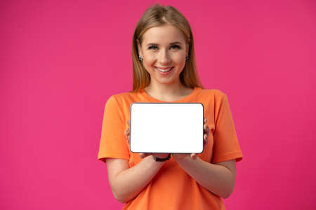 Young caucasian woman pointing her digital tablet with blank screen for your design on color backgroundの写真素材