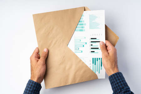 Male hands opening craft paper envelope above white surfaceの写真素材