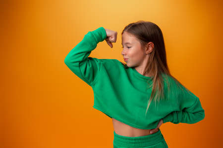 Teen girl showing off muscles biceps against orange backgroundの写真素材