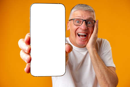Photo of senior surprised man point finger at smartphone over yellow background