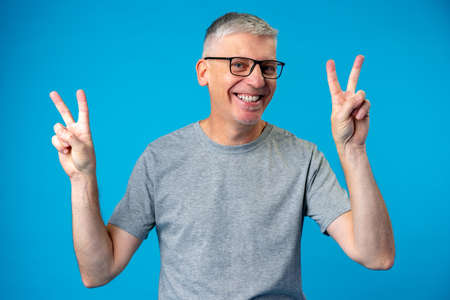 Senior man showing victory sign over blue background