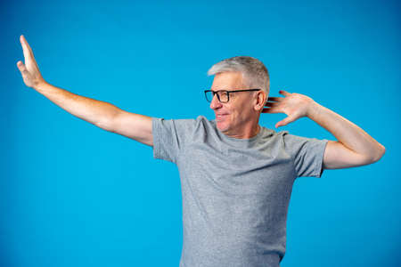 Middle-aged gray-haired man dancing and having fun on blue backgorundの写真素材