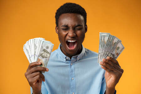 Excited black guy holding stack of Dollars in yellow studio