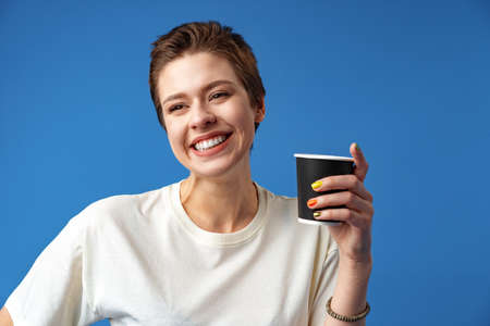 Beautiful smiling woman drinking coffee against blue background
