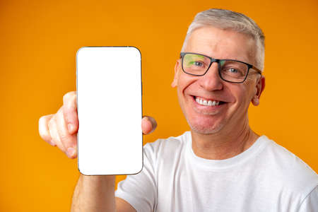 Senior handsome smiling man holding smartphone showing screen over yellow backgroundの写真素材