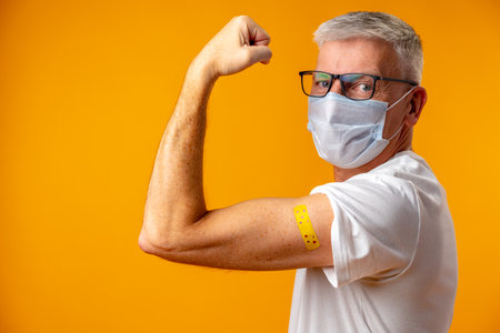 Senior man against yellow background received vaccinationの写真素材