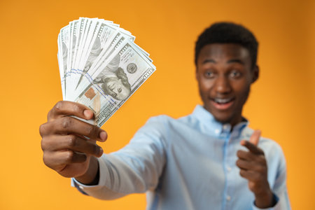 Excited black guy holding stack of Dollars in yellow studio