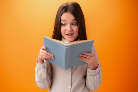 Portrait of clever teen girl with books against orange background