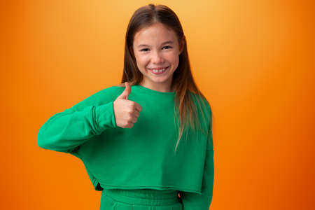 Teen girl making thumb up gesture against orange background