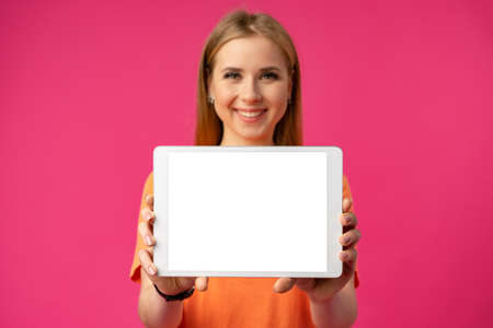 Young Caucasian woman pointing her digital tablet with blank screen for your design on color backgroundの写真素材