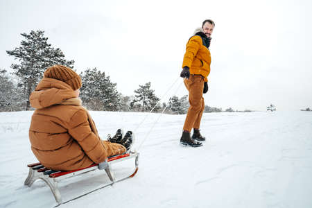 Father pulling little son on sledge in winter