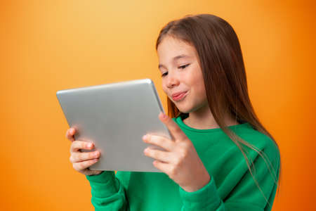 Beautiful teen girl using digital tablet over orange studio background