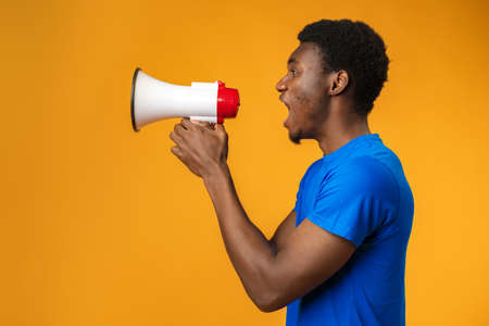 Young black man shouting in megaphone on yellow backgroundの写真素材