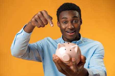 Young african amercian man holding piggy bank over yellow backgroundの写真素材