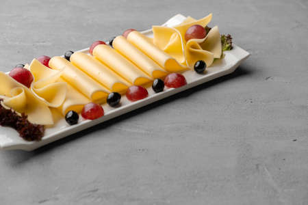 Cheese platter with grapes and black olives on gray background