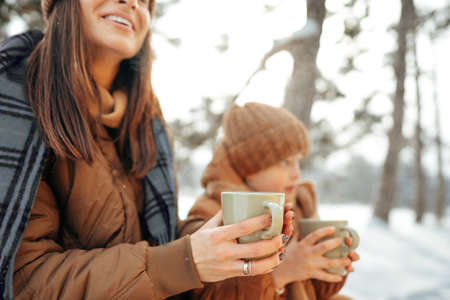 Young woman with a son in winter forest on a picnic drink hot teaの写真素材