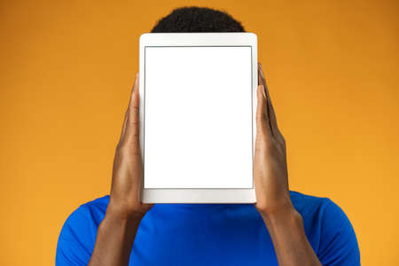 African man showing digital tablet over yellow background.