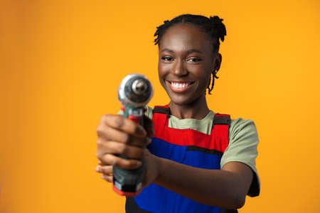 Black African American female model in uniform holding a screwdriver repair tool against yellow backgroundの写真素材