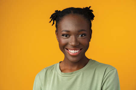 Portrait of beautiful positive african american woman in yellow studioの写真素材