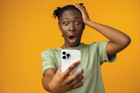 Happy smiling african american girl using her smartphone in yellow studio.の写真素材