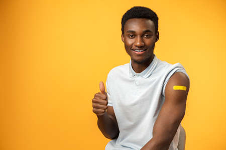 Vaccinated african american man showing his arm against yellow background