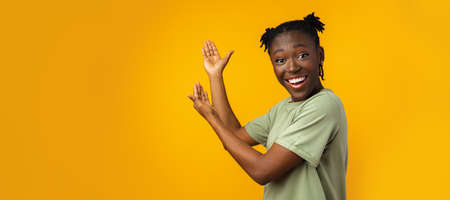 Cheerful Afro woman points to copy space in yellow studioの写真素材