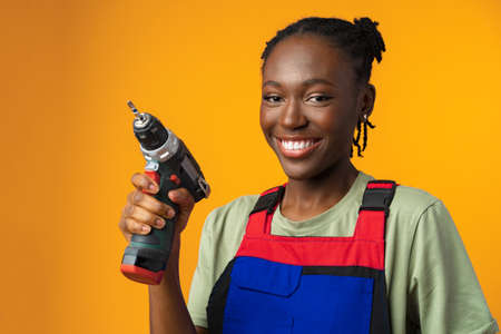 Black African American female model in uniform holding a screwdriver repair tool against yellow backgroundの写真素材