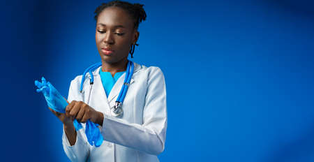 Black female doctor wears sterile blue gloves