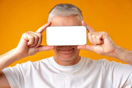 Middle age man holding smartphone on face over yellow backgroundの写真素材