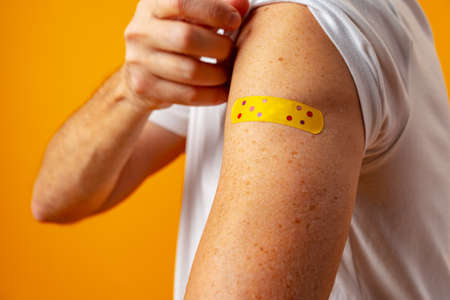 Man showing his shoulder with patch after vaccine against yellow backgroundの写真素材