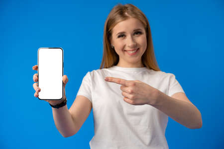 Young woman point finger at isolated smartphone screen over blue color background