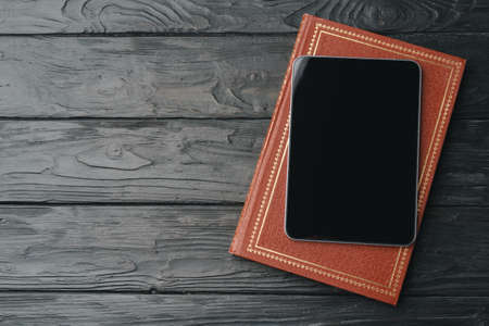 Digital tablet with black screen and book on wooden tableの写真素材