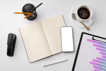 Creative white table with blank cellphone and supplies