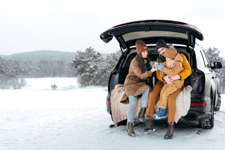 Winter portrait of a family sit on car trunk enjoy their vacation in forestの写真素材
